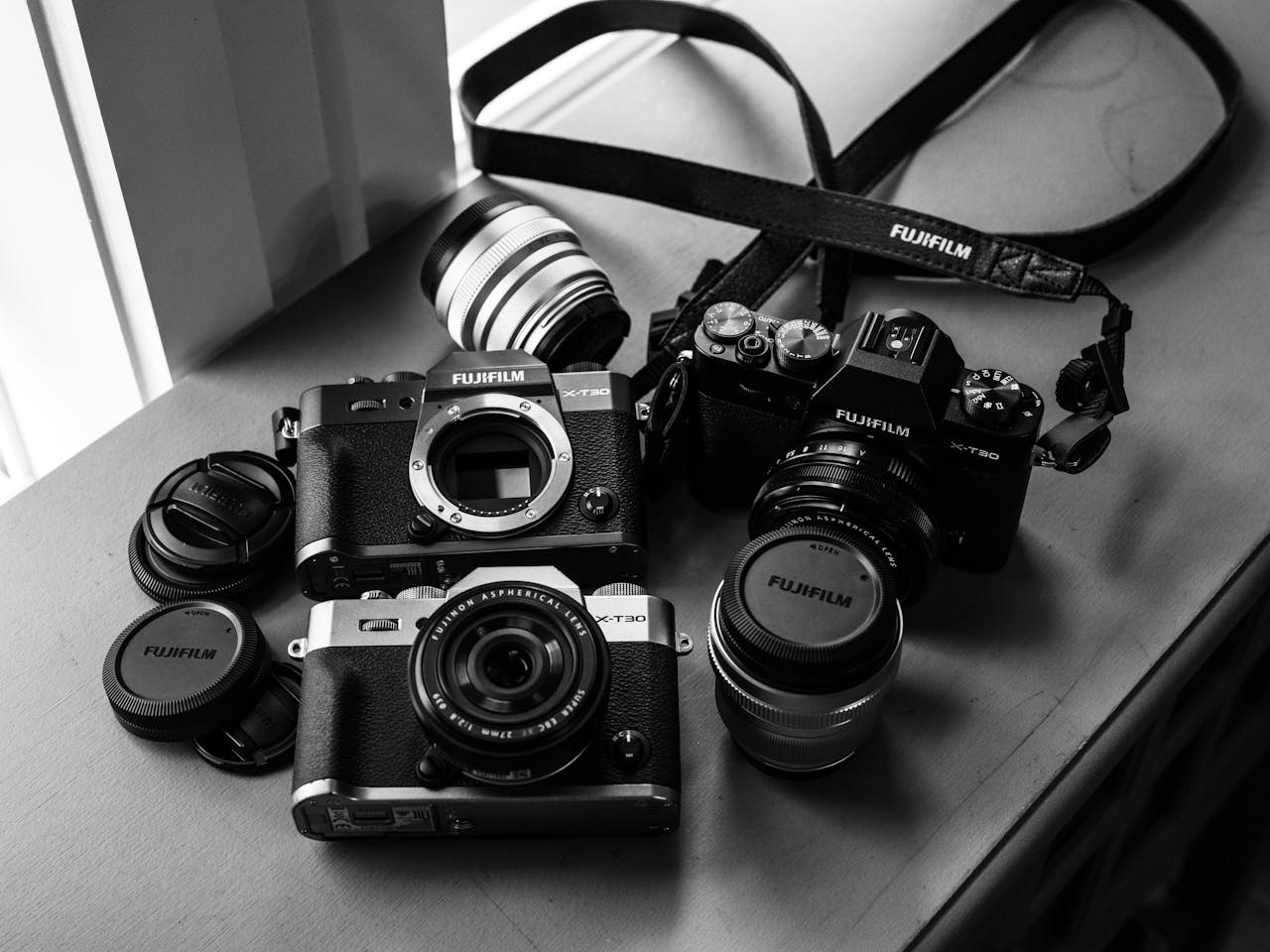 A collection of vintage Fujifilm analog cameras and lenses displayed on a table in monochrome.